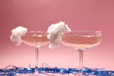 Tasty cocktails in glasses decorated with cotton candy and blue shiny streamers on pink background, closeup