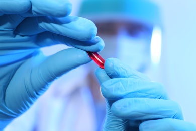 Photo of Scientist in protective gloves holding pill, focus on hand