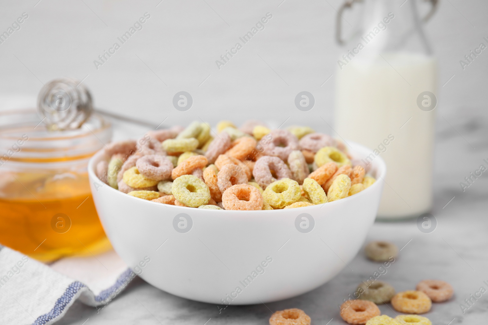 Photo of Tasty cereal rings in bowl, milk and honey on light table, closeup