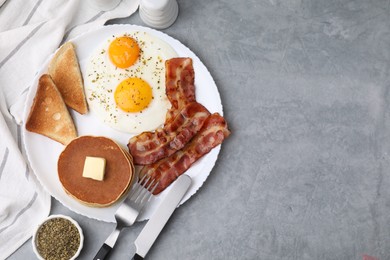 Tasty pancakes served with fried eggs and bacon on grey table, flat lay. Space for text