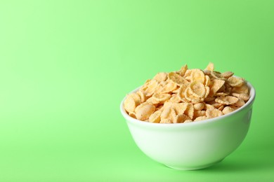 Photo of Bowl of tasty crispy corn flakes on light green background, space for text