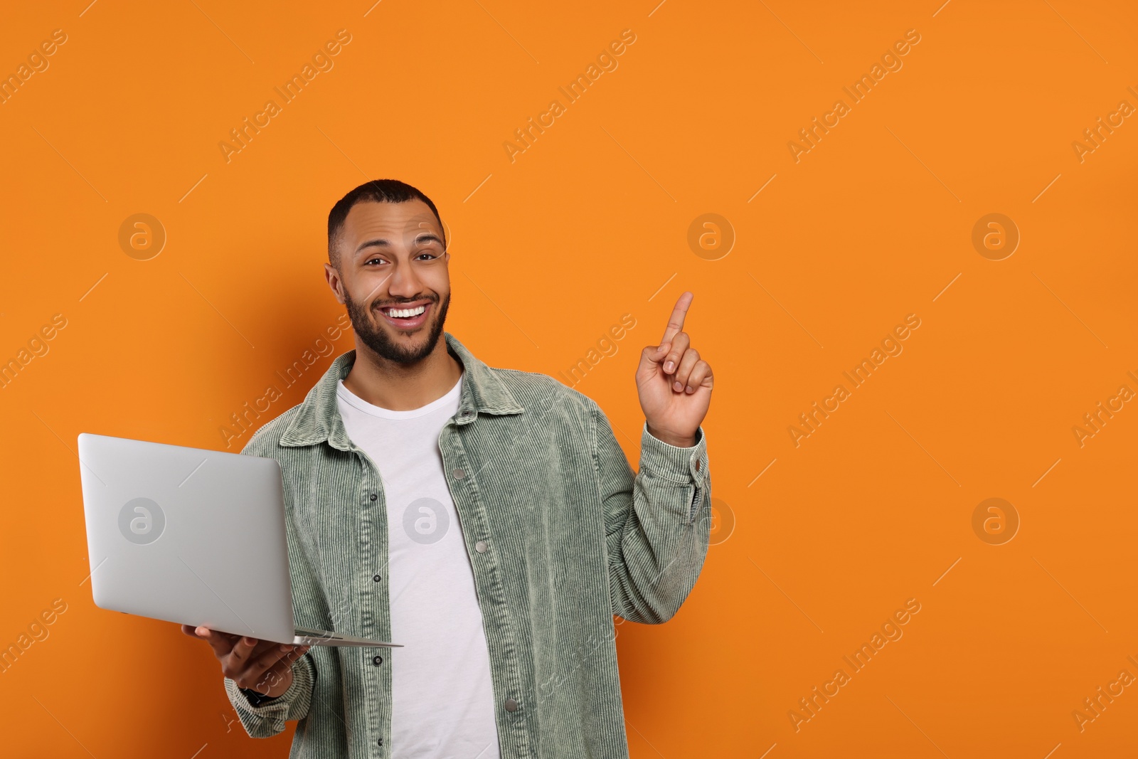 Photo of Smiling young man with laptop near orange wall, space for text