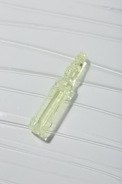 Skincare ampoule on white surface covered with gel, above view