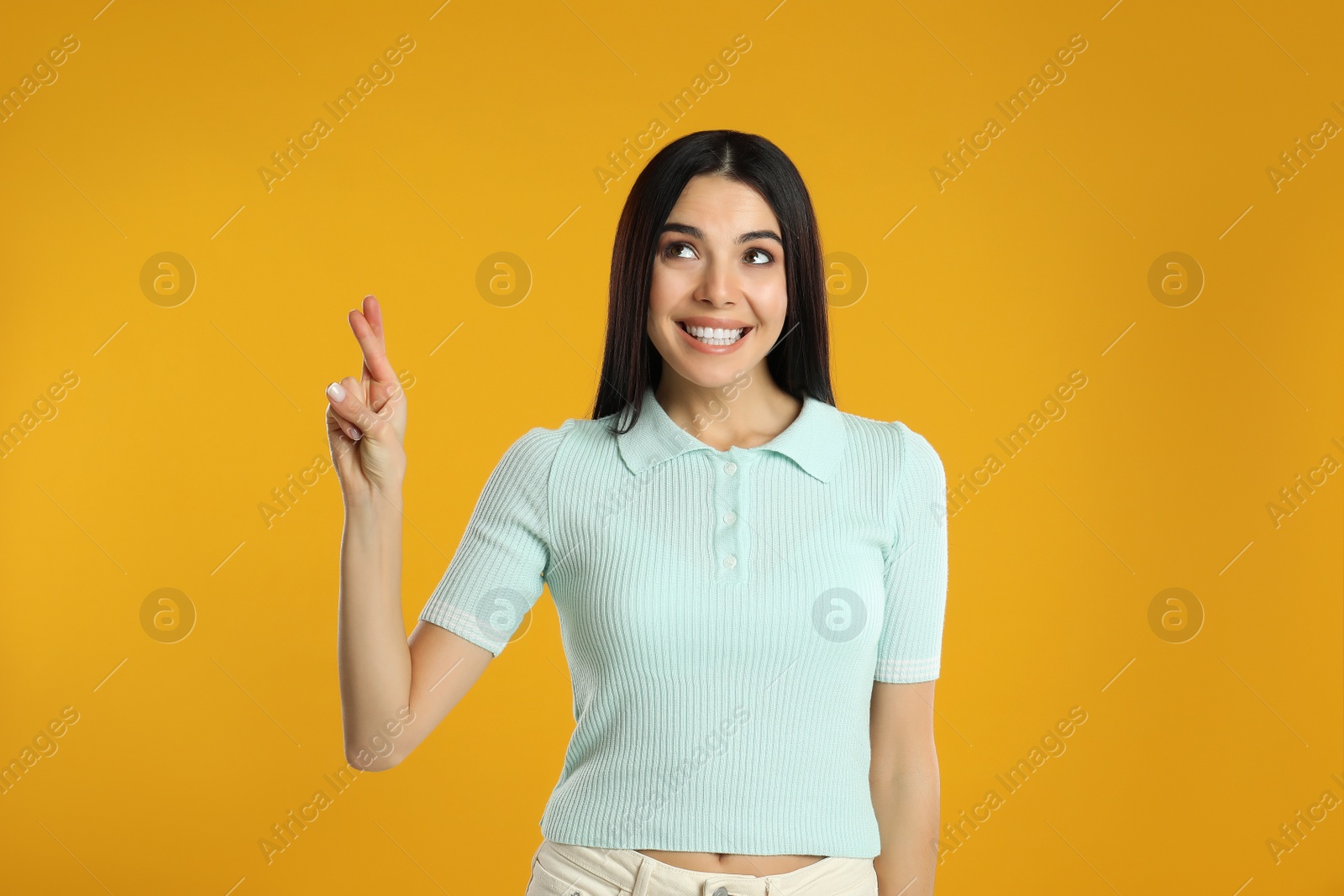 Photo of Woman with crossed fingers on yellow background. Superstition concept