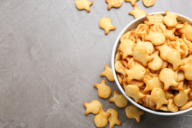 Photo of Delicious goldfish crackers in bowl on grey table, flat lay. Space for text