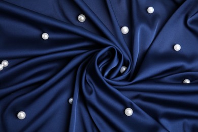 Photo of Many beautiful pearls on delicate dark blue silk, flat lay