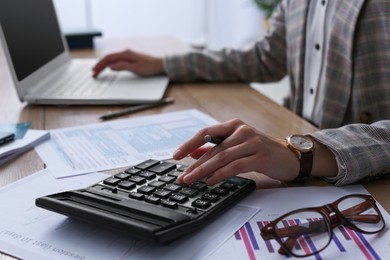 Photo of Tax accountant with calculator working at table in office, closeup