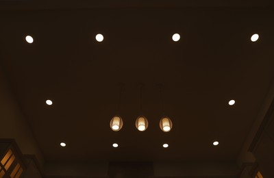 Ceiling with modern lamps in stylish room at night, low angle view