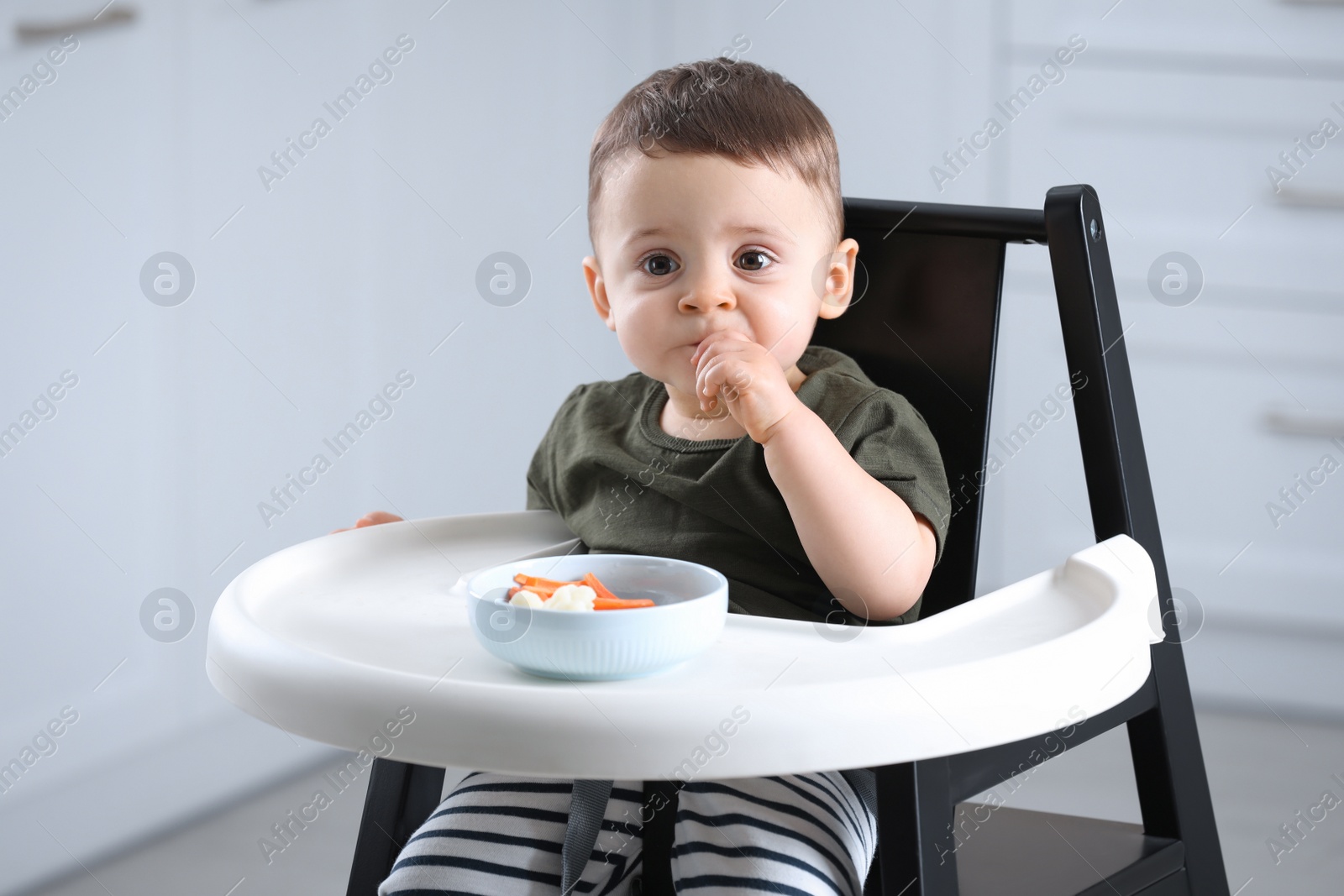 Photo of Cute little baby eating healthy food in high chair at home