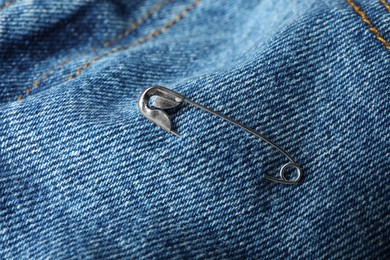 Metal safety pin on denim fabric, closeup