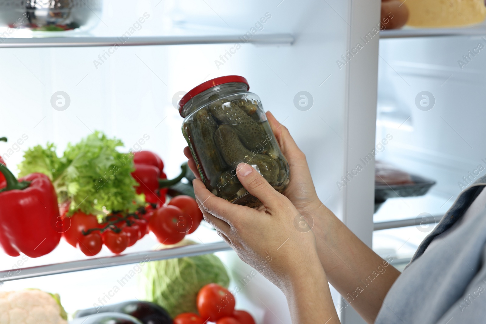 Photo of Young woman taking jar of pickles out of refrigerator, closeup