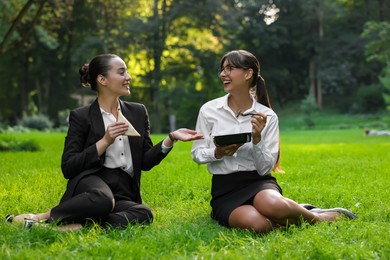 Photo of Happy colleagues having business lunch on green grass in park
