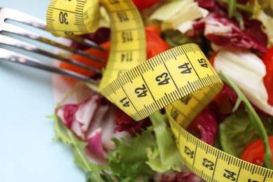 Photo of Healthy salad with measuring tape on light blue plate, closeup. Diet concept