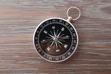 Photo of One compass on wooden table, top view. Tourist equipment