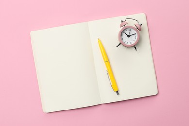 Photo of Ballpoint pen, notebook and alarm clock on pink background, top view