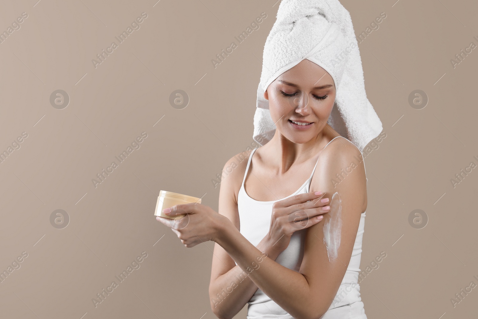 Photo of Happy woman applying body cream onto arm on beige background, space for text