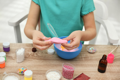 Photo of Little girl making DIY slime toy at table indoors, closeup