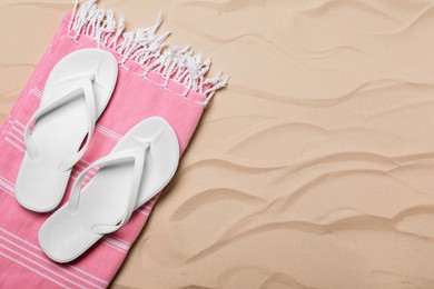 Pair of white flip flops and blanket on sand, top view. Space for text