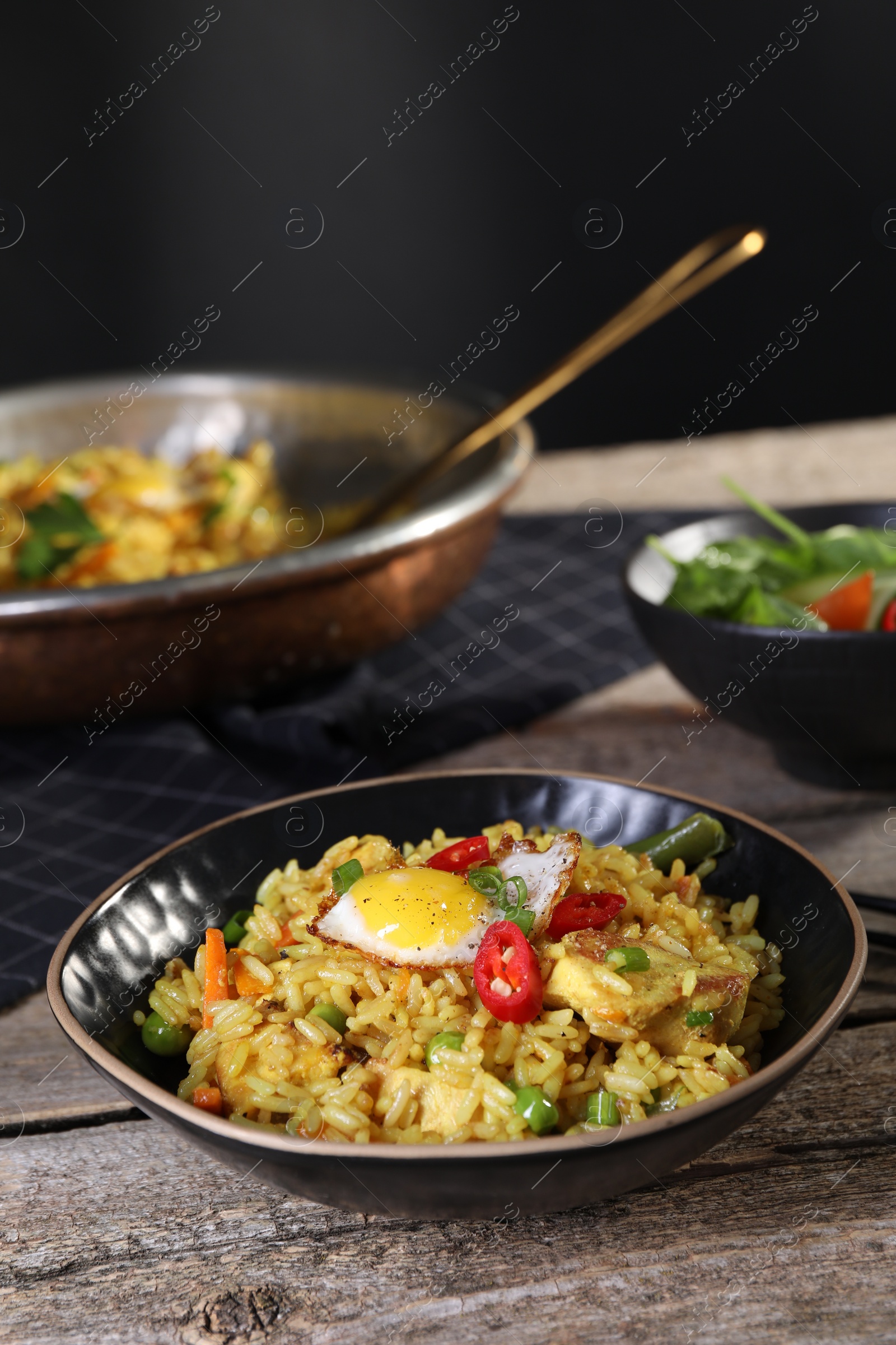 Photo of Tasty rice with meat, egg and vegetables in bowl on wooden table