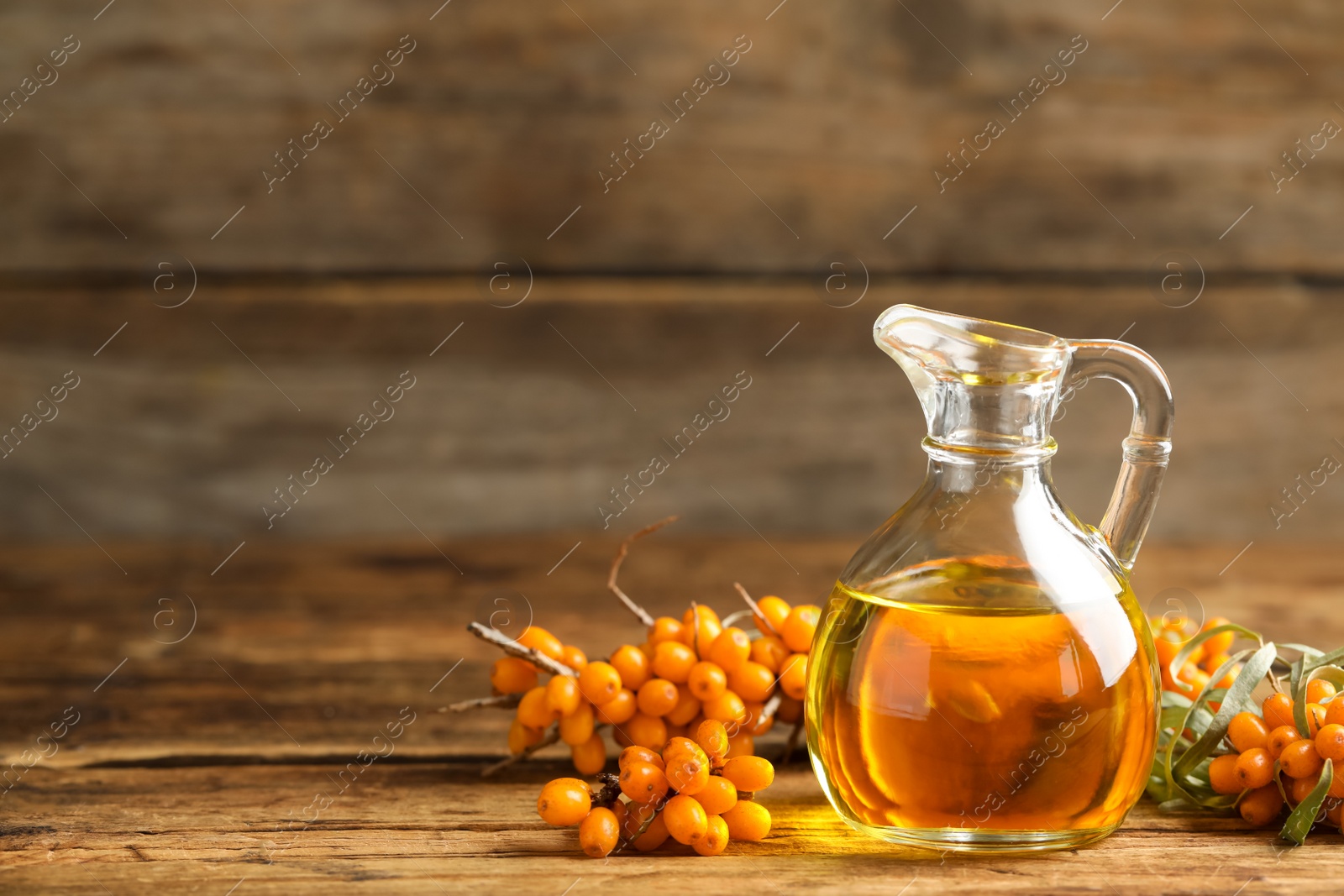 Photo of Natural sea buckthorn oil and fresh berries on wooden table. Space for text