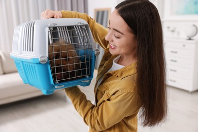 Photo of Travelling with pet. Smiling woman looking at carrier with her dog indoors