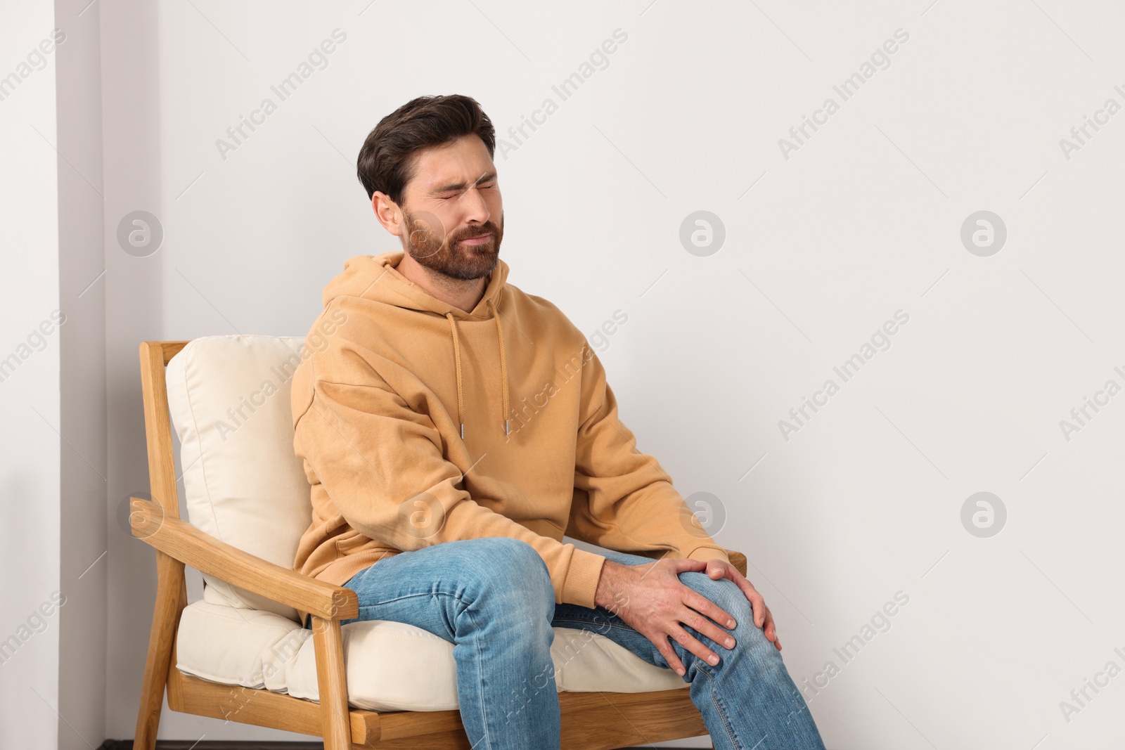 Photo of Man suffering from leg pain and touching knee on soft armchair indoors, space for text