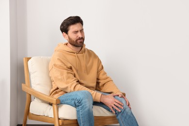 Photo of Man suffering from leg pain and touching knee on soft armchair indoors, space for text
