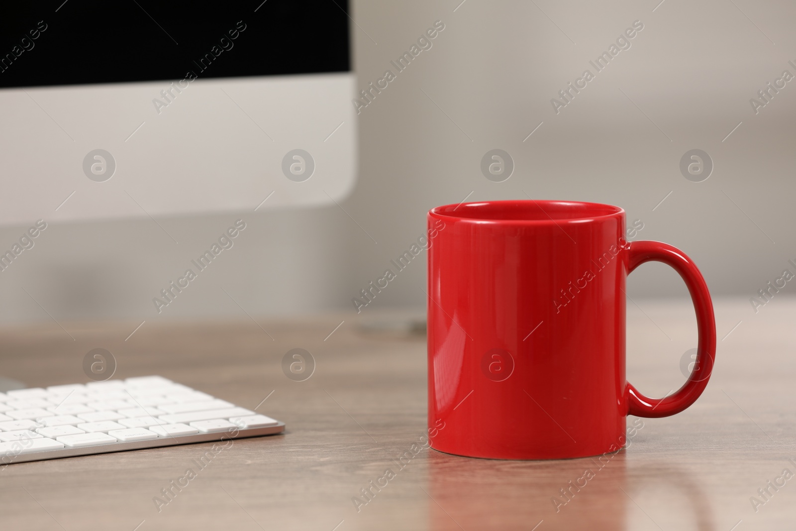 Photo of Red ceramic mug and computer on wooden table at workplace. Space for text