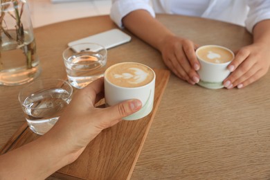 Friends drinking coffee at wooden table in cafe, closeup