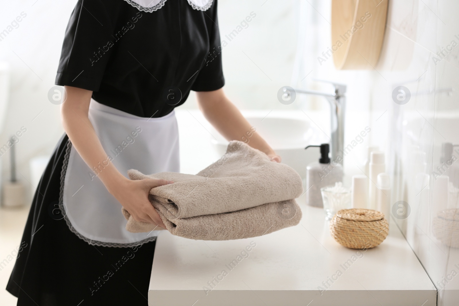 Photo of Young chambermaid putting stack of fresh towels on countertop in bathroom, closeup