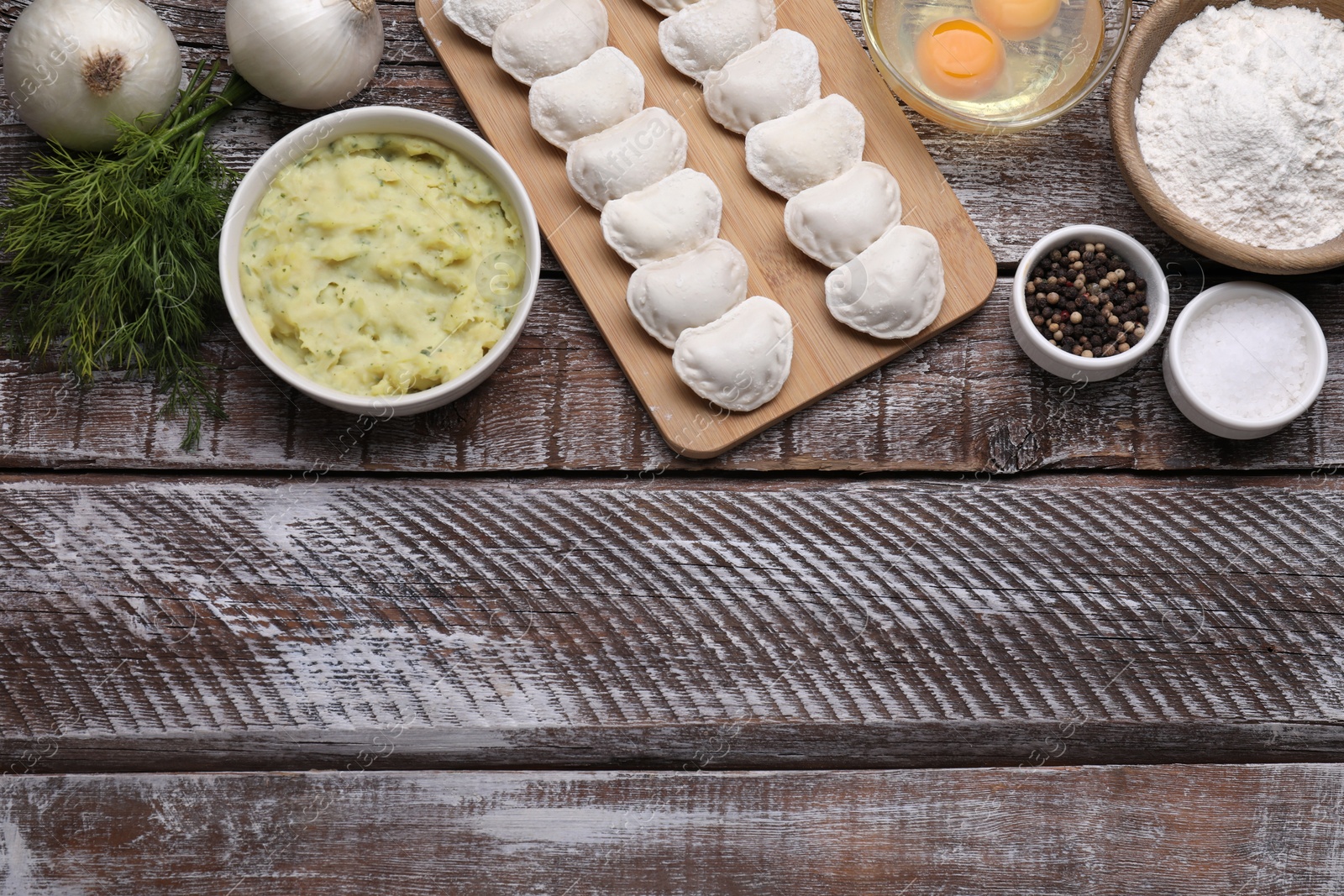 Photo of Raw dumplings (varenyky) and ingredients on wooden table, flat lay. Space for text