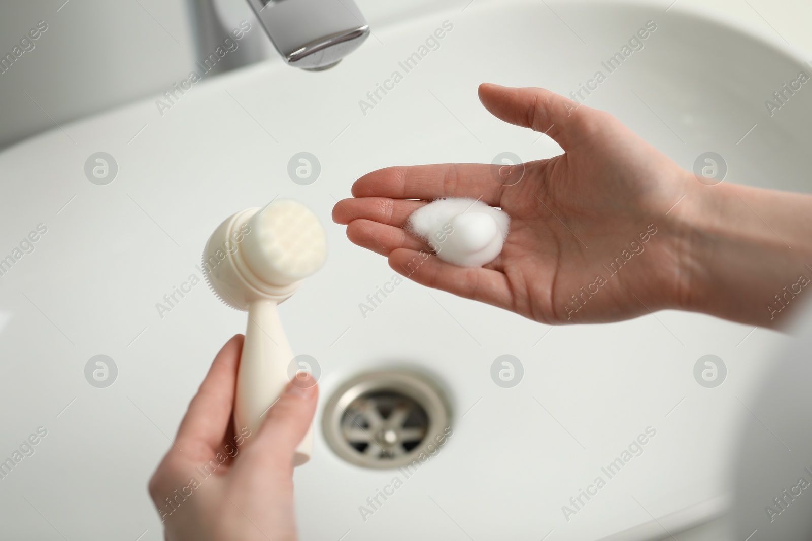 Photo of Washing face. Woman with brush and cleansing foam above sink in bathroom, closeup