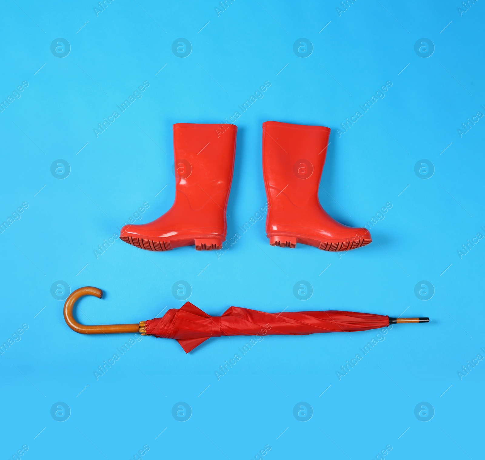 Photo of Beautiful red umbrella and rubber boots on blue background, flat lay