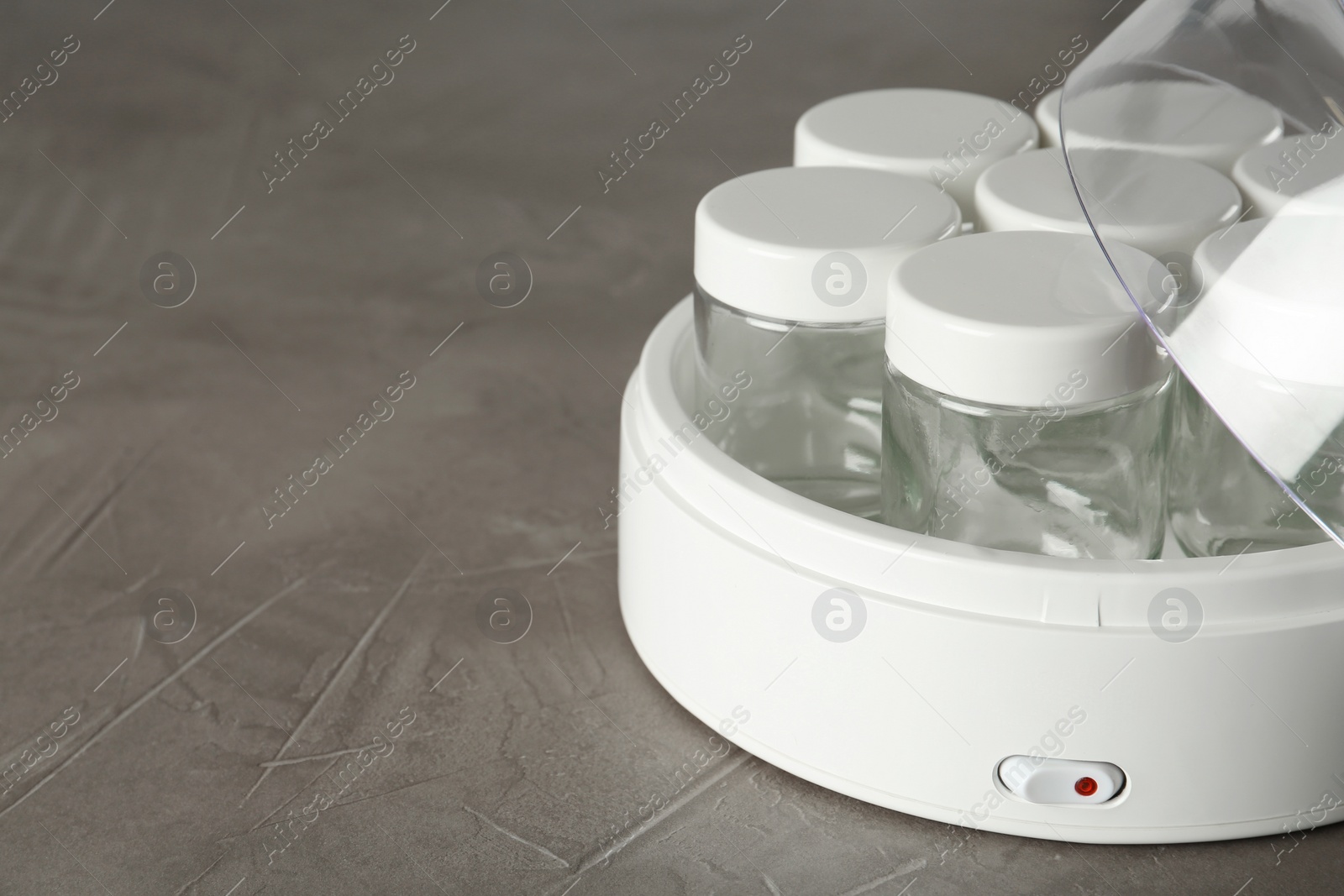 Photo of Modern yogurt maker with empty jars on grey table, closeup. Space for text