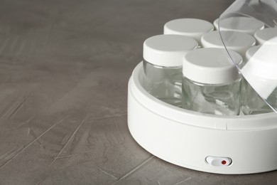 Modern yogurt maker with empty jars on grey table, closeup. Space for text