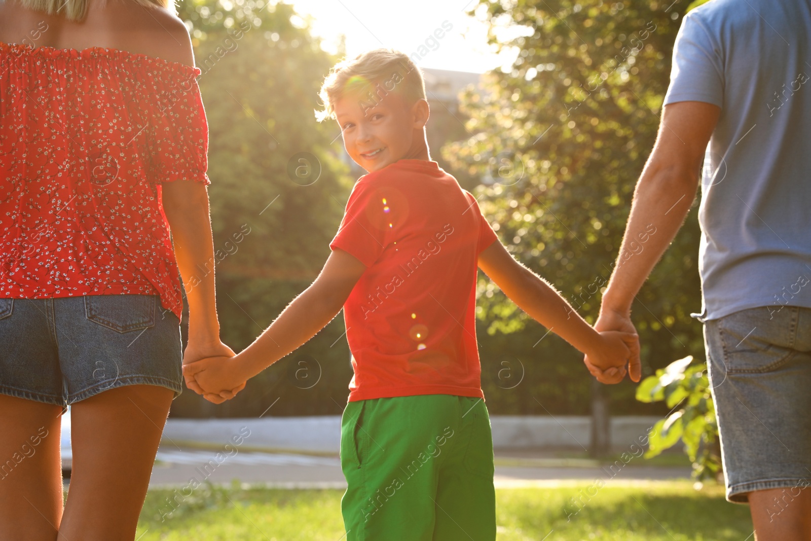 Photo of Little boy and his parents holding hands outdoors. Family weekend