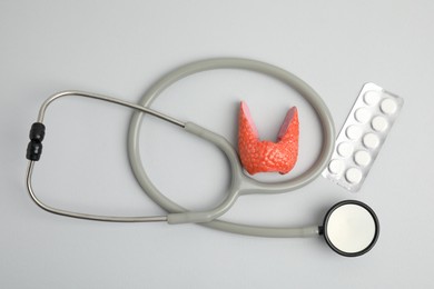 Photo of Plastic model of healthy thyroid, pills and stethoscope on grey background, flat lay