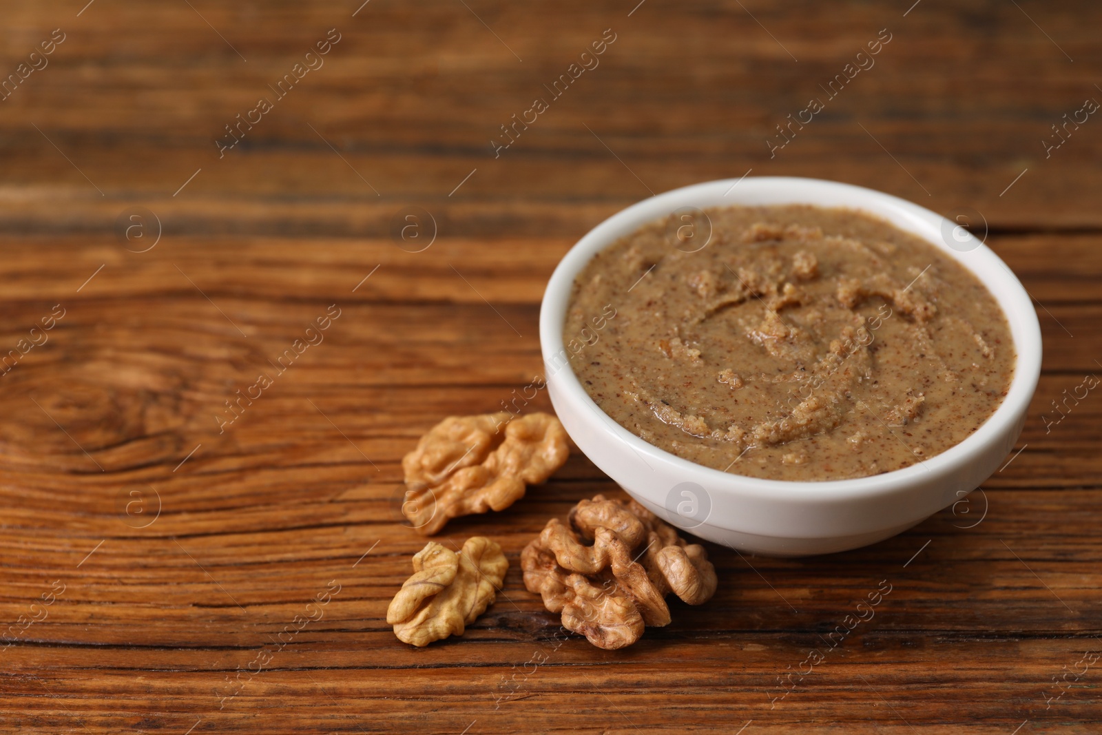 Photo of Delicious nut butter in bowl and walnuts on wooden table, closeup. Space for text