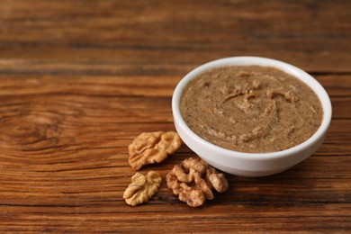 Delicious nut butter in bowl and walnuts on wooden table, closeup. Space for text