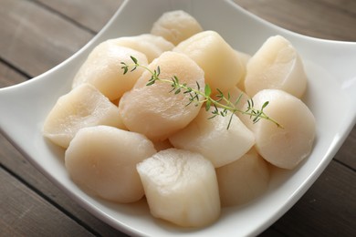 Photo of Fresh raw scallops and thyme in bowl on wooden table, closeup