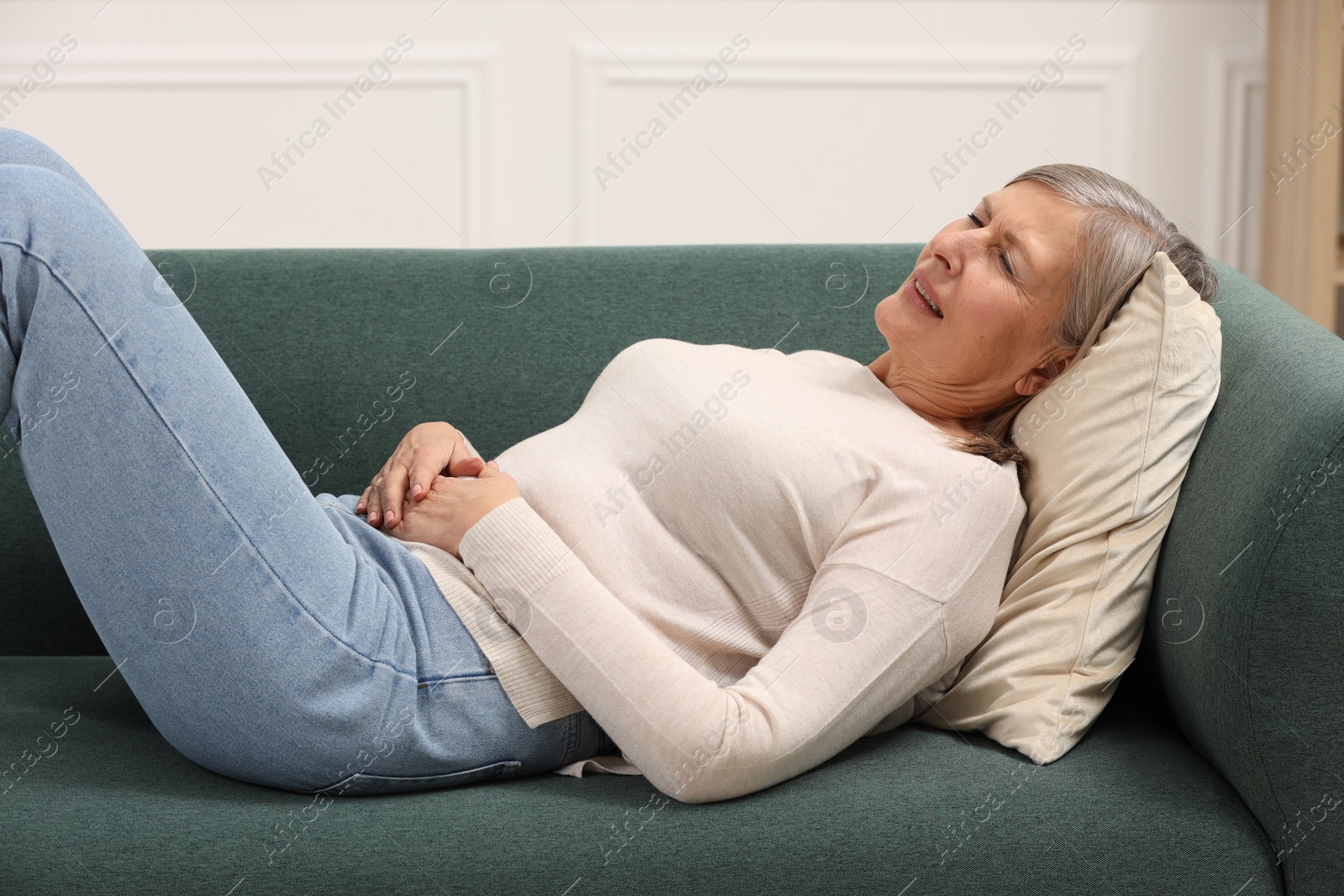 Photo of Menopause. Woman suffering from abdominal pain on sofa at home