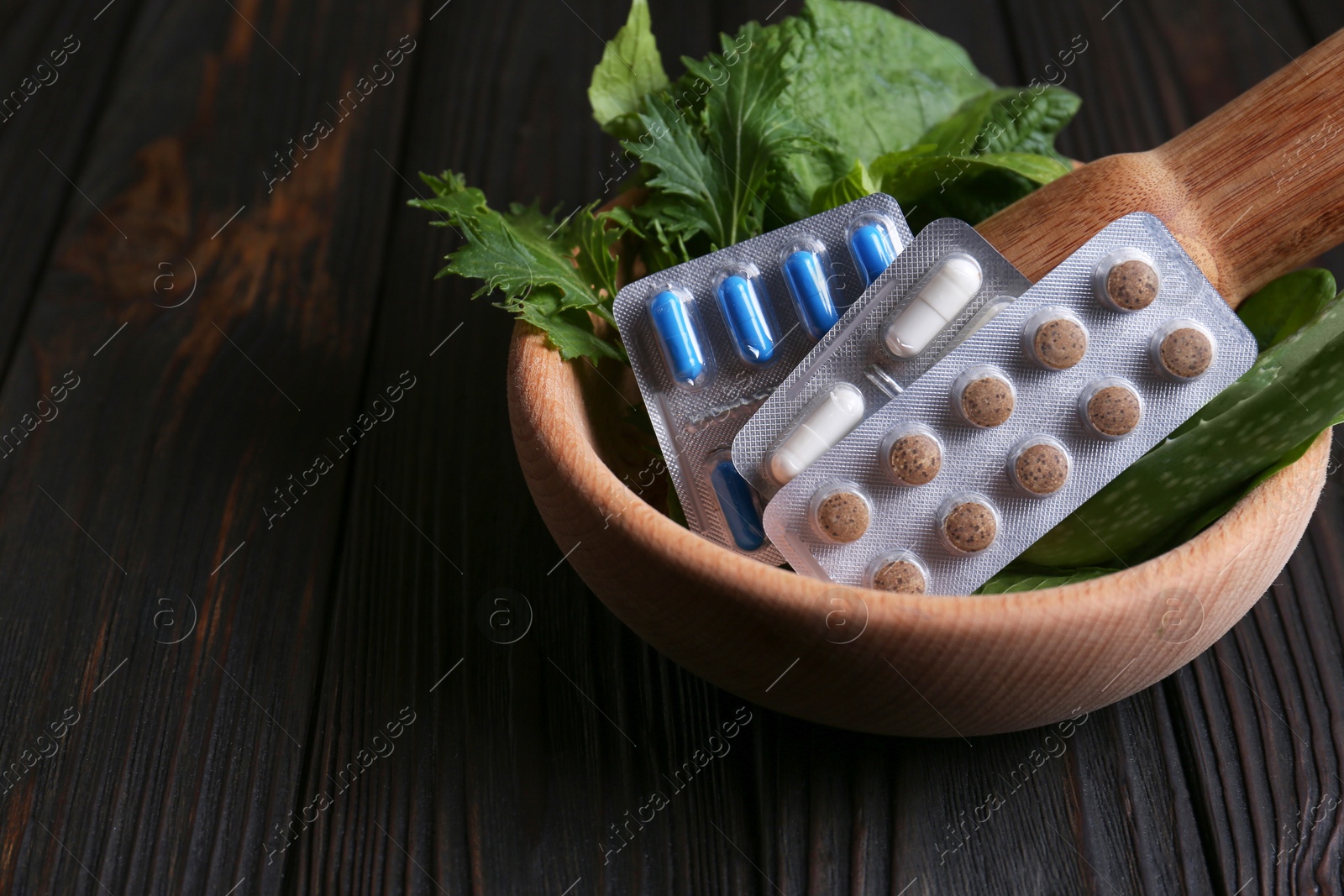 Photo of Mortar with fresh green herbs and pills on wooden table, closeup. Space for text