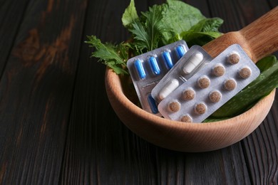 Mortar with fresh green herbs and pills on wooden table, closeup. Space for text