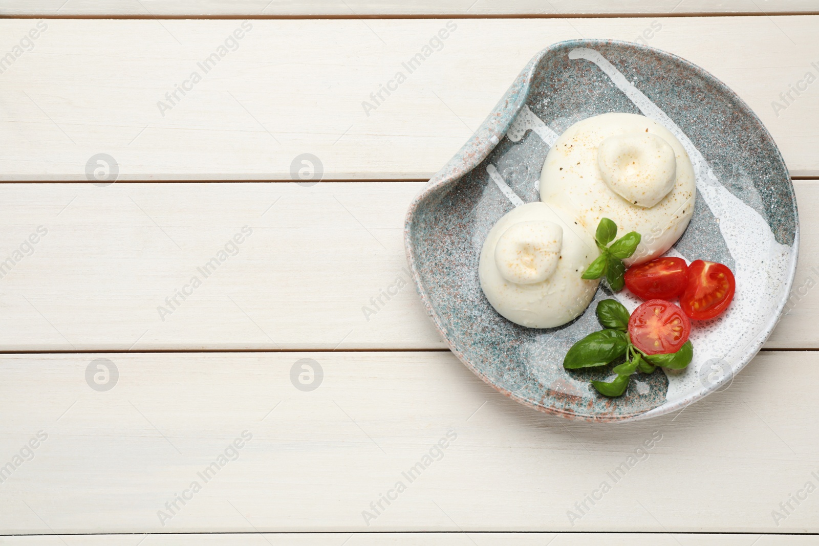 Photo of Delicious burrata cheese with basil and tomatoes on white wooden table, top view. Space for text