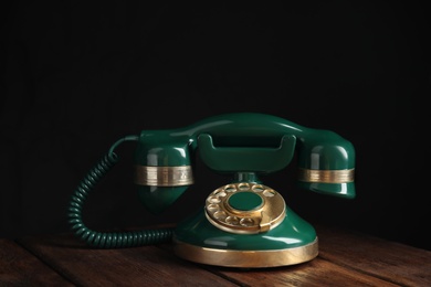 Vintage corded phone on wooden table against black background