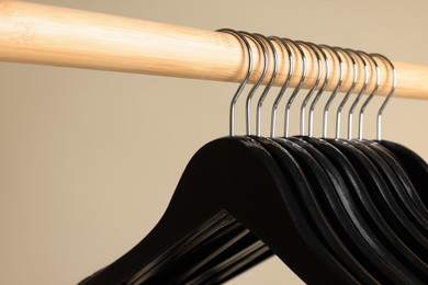 Photo of Black clothes hangers on wooden rail against beige background, closeup