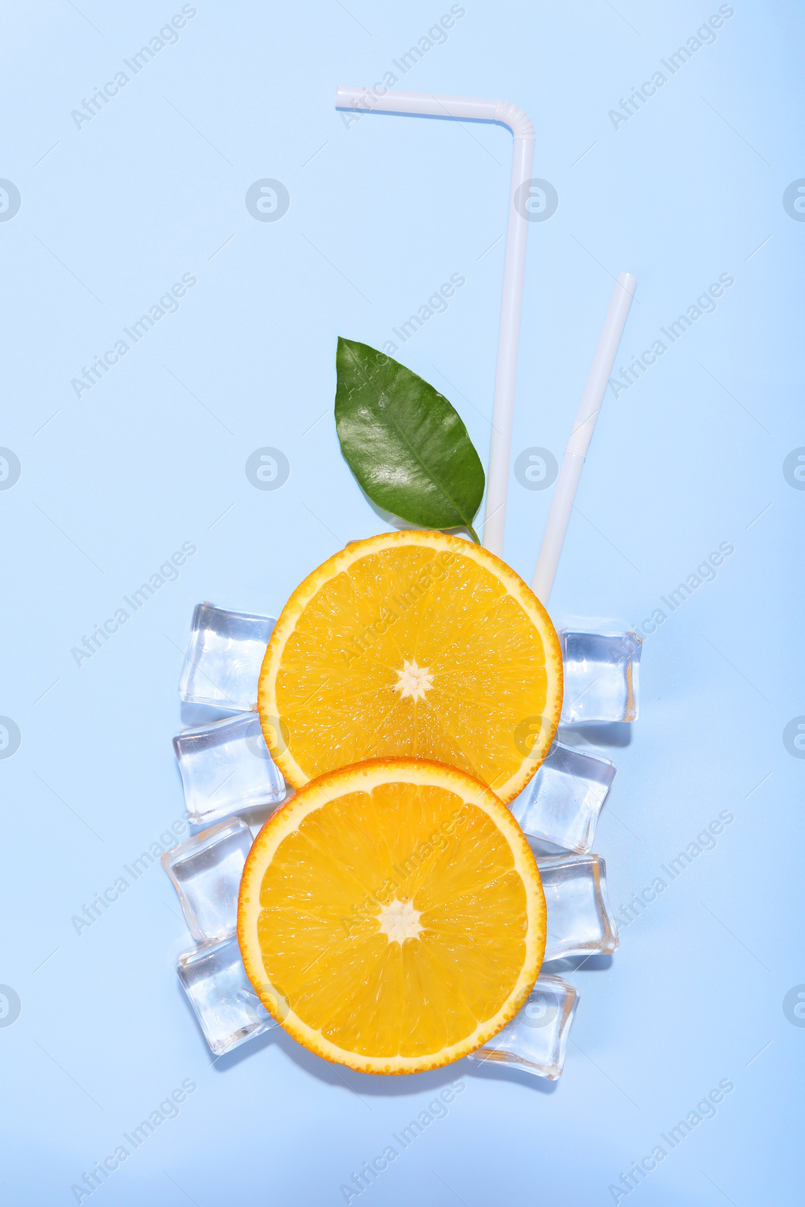 Photo of Slices of juicy orange, ice cubes and leaf on light blue background, flat lay