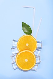Slices of juicy orange, ice cubes and leaf on light blue background, flat lay