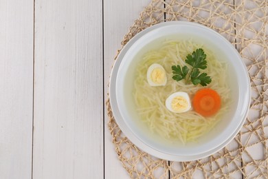 Photo of Tasty soup with noodles, egg, carrot and parsley in bowl on white wooden table, top view. Space for text