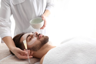 Photo of Cosmetologist applying mask on client's face in spa salon